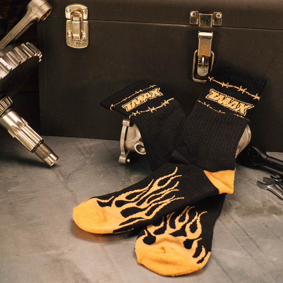 Black and gold Flames Forever socks with flame graphics displayed beside a workbench